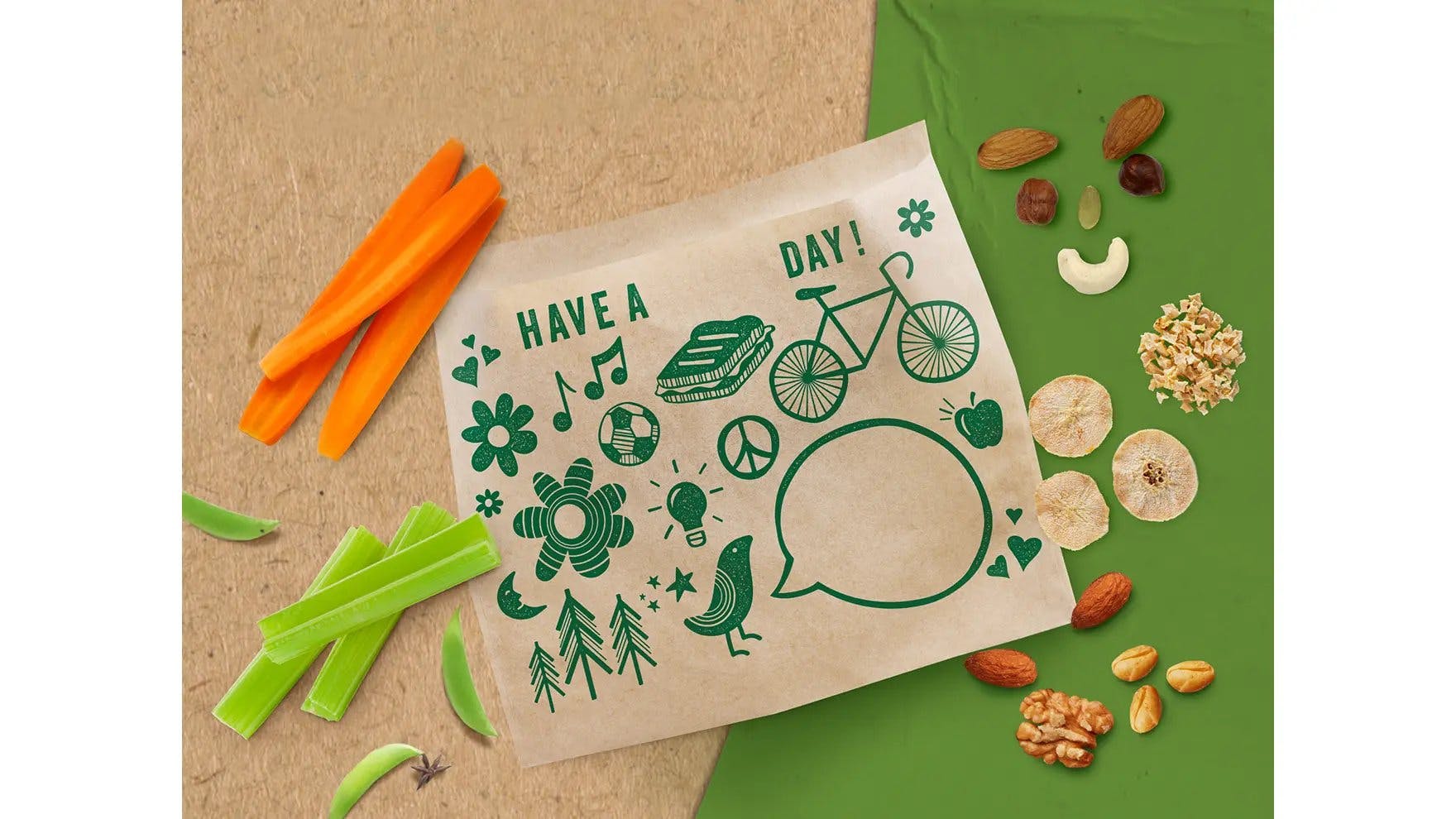 A Ziploc® brand recycleable paper bag surrounded by carrots, celery, nuts, and dried fruits