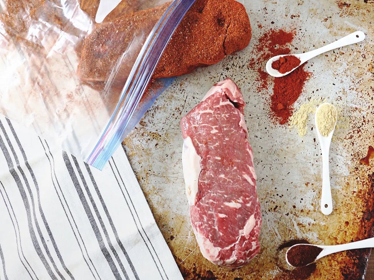 Smoked paprika dry-rubbed steaks in Ziplog bag with teaspoons of spices