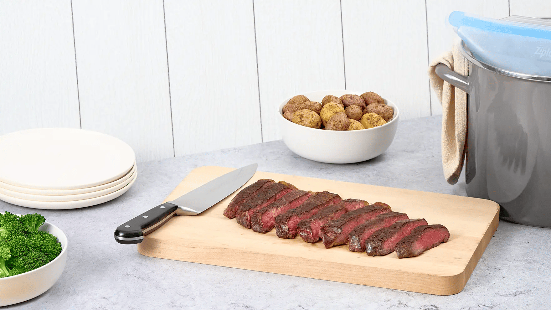 Bifteck de surlonge sous vide tranché sur une planche à découper, à côté d’une casserole et de bols de légumes