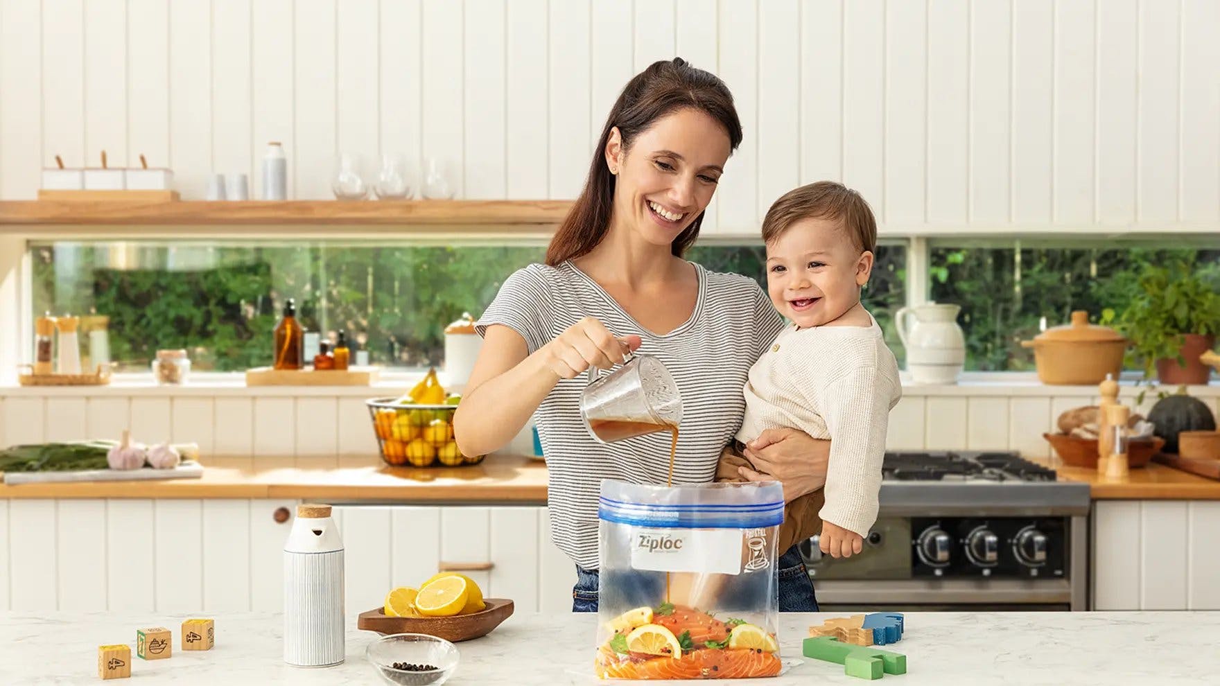 Mother holding a baby and pouring marinade into a Ziploc bag of salmon